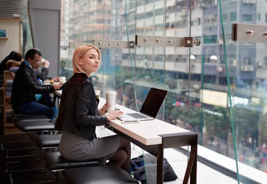 Woman working on a laptop at a coffee shop while looking out of a window.