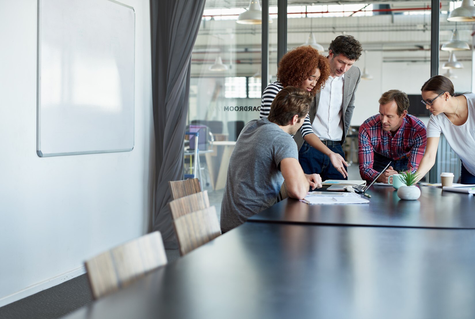 Group of people in a conference room all looking at a laptop.